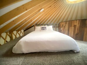 Una cama en un dormitorio tipo altillo con techo inclinado y vigas de madera.