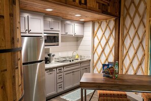 Une cuisine avec des meubles blancs, des appareils en acier inoxydable, une table en bois et un mur orné d’un motif.