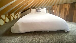 A bed in a loft bedroom with a sloped ceiling and wooden beams.