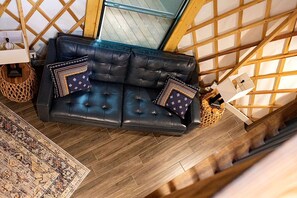 Un salon moderne avec un canapé en cuir, des coussins à motifs, un panier en osier et un plancher en bois.