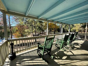 A covered porch with wooden railings and green chairs. - Spacious Waterfront Cabin Overlooking Private Pond near Zwolle, Louisiana (Zwolle)