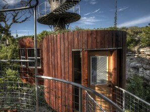 Une cabane en bois avec un escalier en colimaçon, une porte dotée d’une fenêtre et une rambarde en métal.