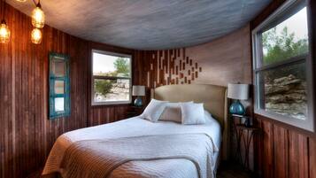 Un dormitorio con pared de madera, una cama con ropa de cama blanca, dos lámparas de noche y una ventana con vistas a árboles.