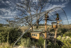 A treehouse with a metal bridge, surrounded by trees and vegetation.