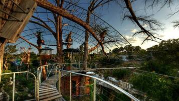 A wooden suspension bridge with metal railings, surrounded by trees and a clear sky.