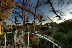 A wooden suspension bridge with metal railings, surrounded by trees and a clear sky.