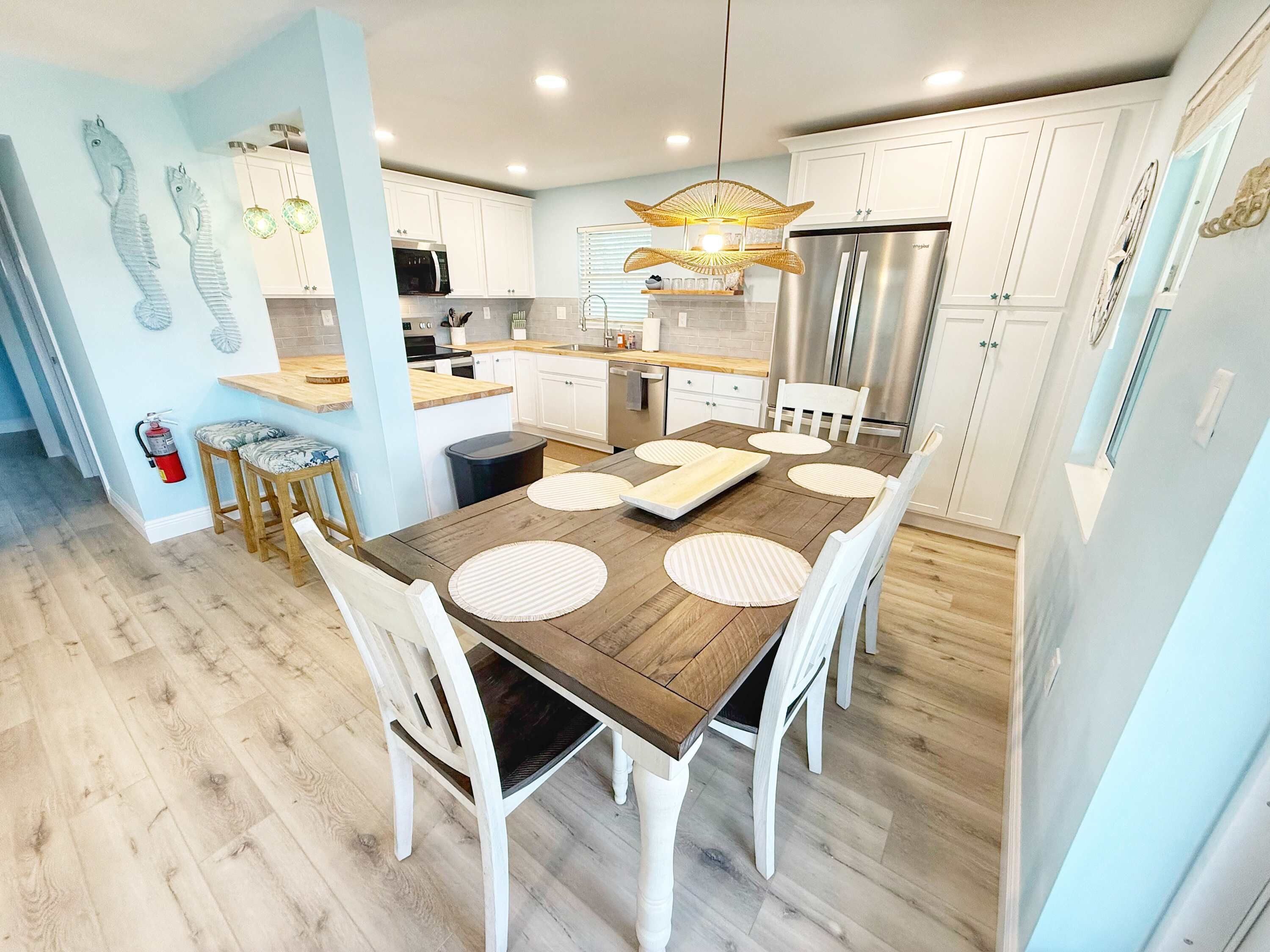 Une cuisine moderne avec des meubles blancs, un réfrigérateur en acier inoxydable et une table à manger en bois agrémentée de sets de table.
