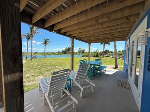 A covered outdoor seating area with tables and chairs, overlooking a body of water and palm trees. - Fun Oceanfront 2 Bedroom Villa with Private Beach Access in Cocoa Beach (Cocoa Beach)