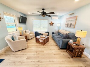A living room with a ceiling fan, a large window with blinds, a TV mounted on the wall, and a star decoration.
