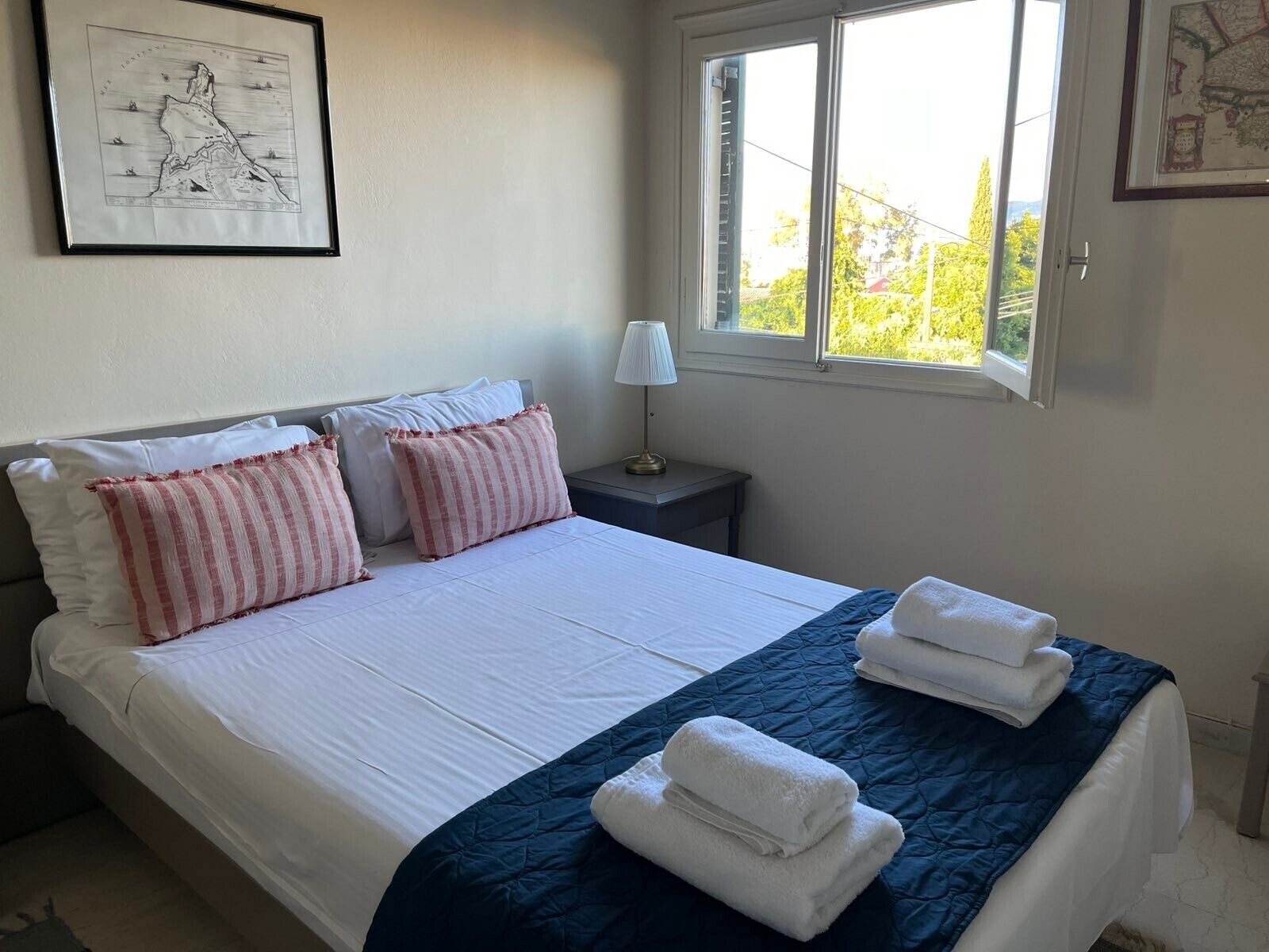 Un lit bien fait, avec des oreillers rayés blancs et roses, une courtepointe bleue et des serviettes pliées posées sur un couvre-lit bleu foncé.
