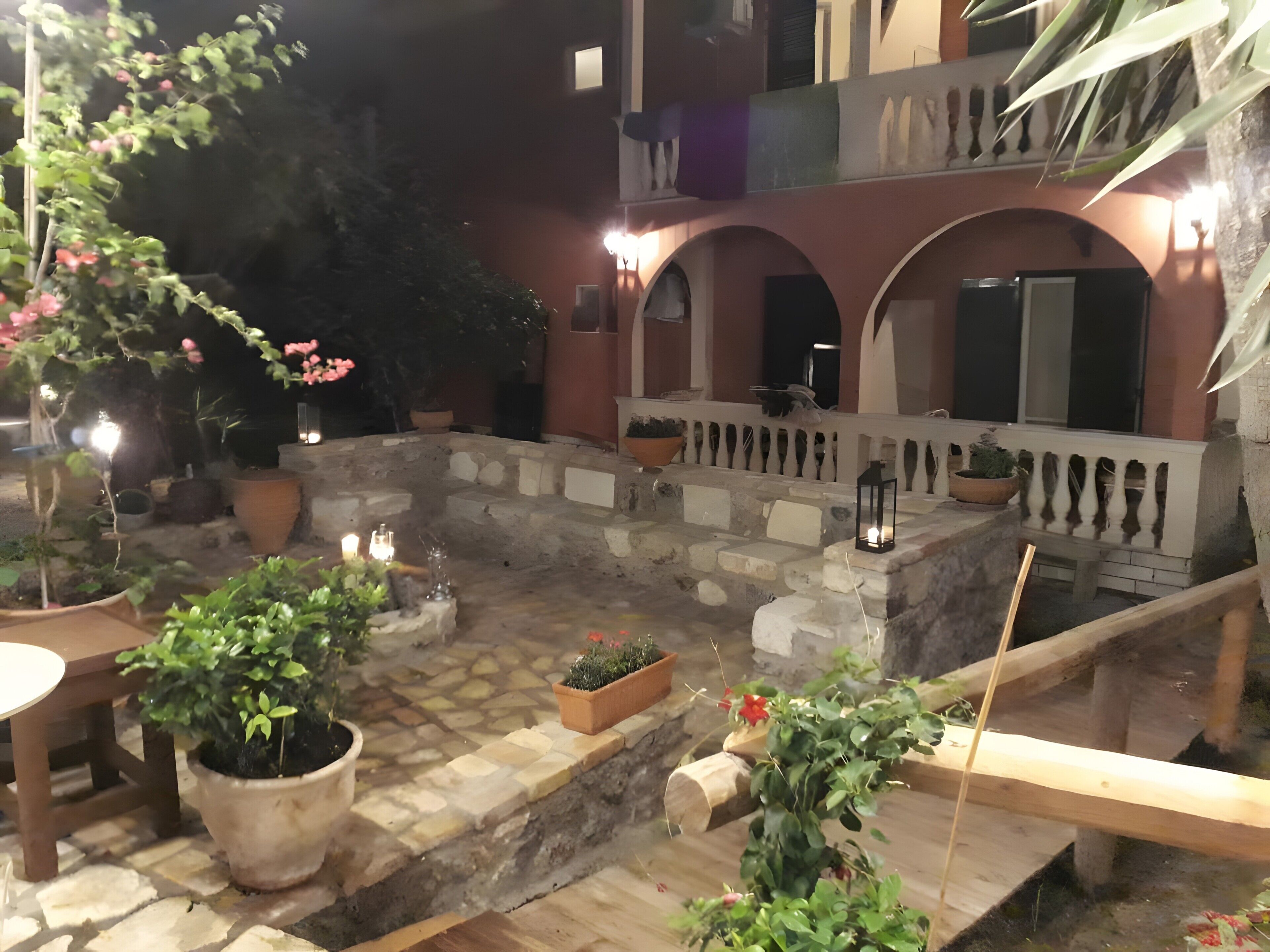Une cour avec des plantes en pot, un banc en pierre et une table en bois.
