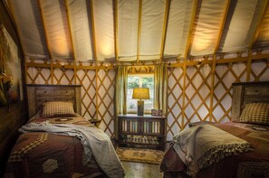 A cozy interior with two beds, a window with curtains, and a wooden bench.