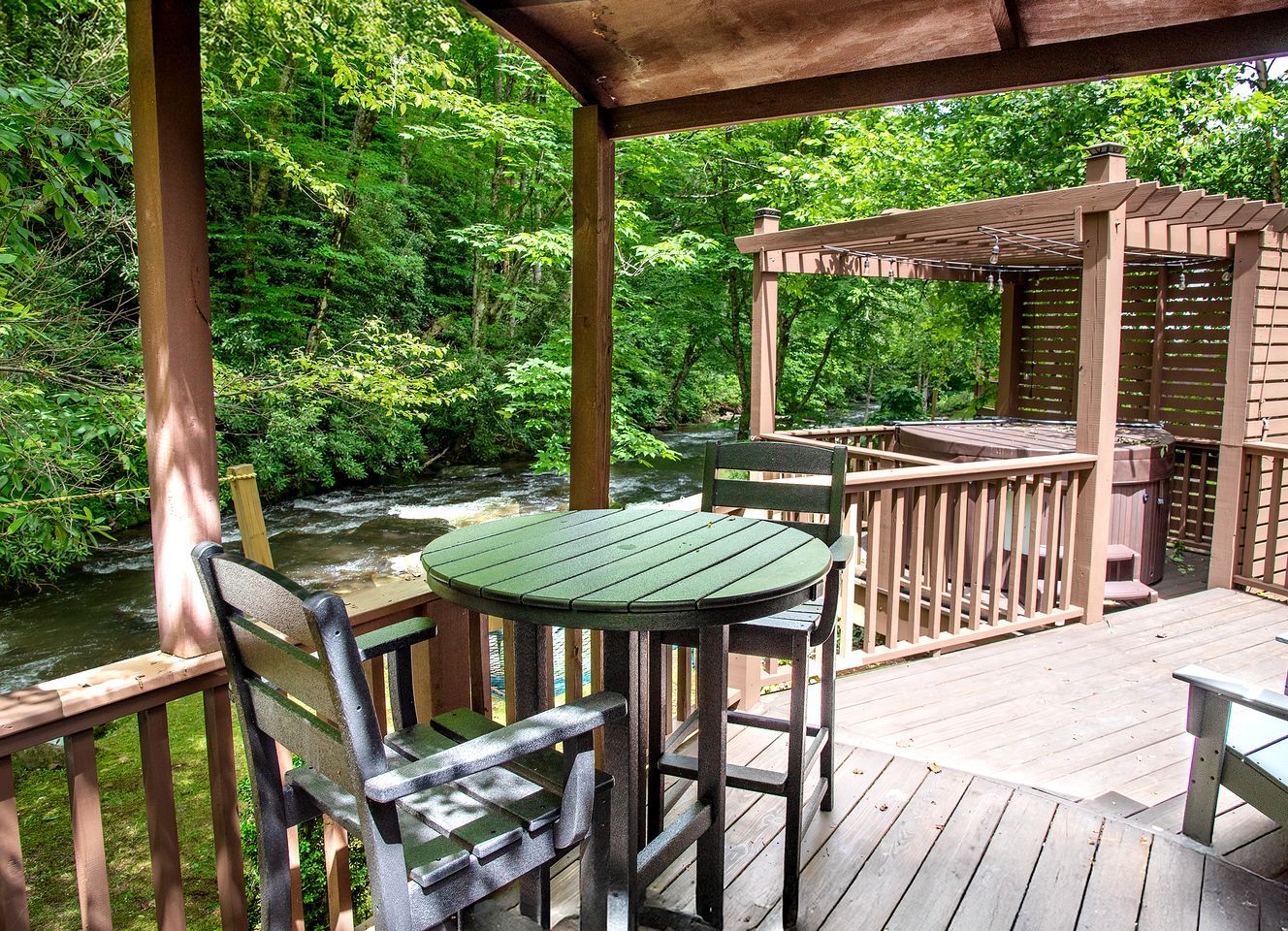 A wooden deck with a table and chairs, overlooking a river.