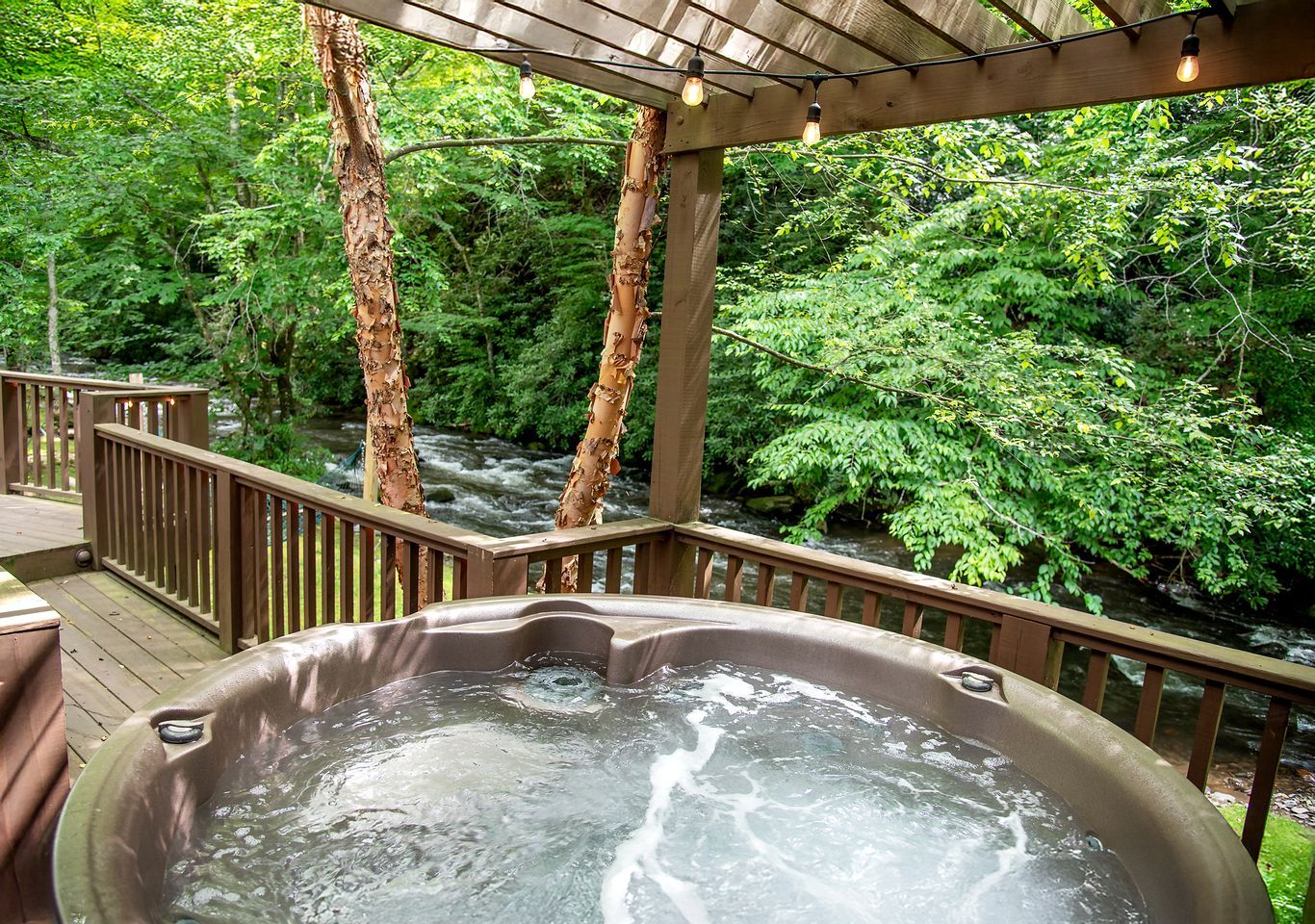 A hot tub on a wooden deck with a view of a river and forest.