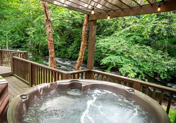 A hot tub on a wooden deck with a view of a river and forest.