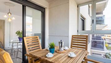 Un balcón con una mesa de madera, sillas y una cafetera.