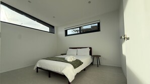 Quarto moderno com cama, mesinha de cabeceira, janela e porta.