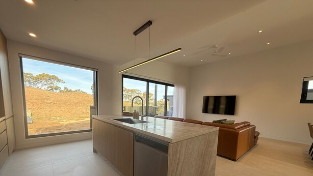 Cozinha moderna com uma ilha grande, área de jantar com sofá e TV na parede.