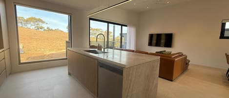 A modern kitchen with a large island, a dining area with a sofa, and a TV mounted on the wall.