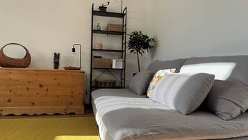 A room with a grey sofa, wooden dresser, metal shelving unit, and a yellow rug.