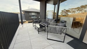Eine moderne Terrassengestaltung mit schwarzem Geländer, einer Glastür und einer Sitzecke mit zwei Sofas und einem Tisch.