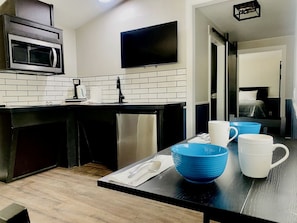 A modern kitchen with a microwave, a flat-screen TV, and a dining area with blue and white bowls.