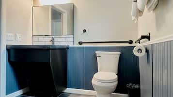 A bathroom with a white toilet, a mirror, a sink, and a towel rack.