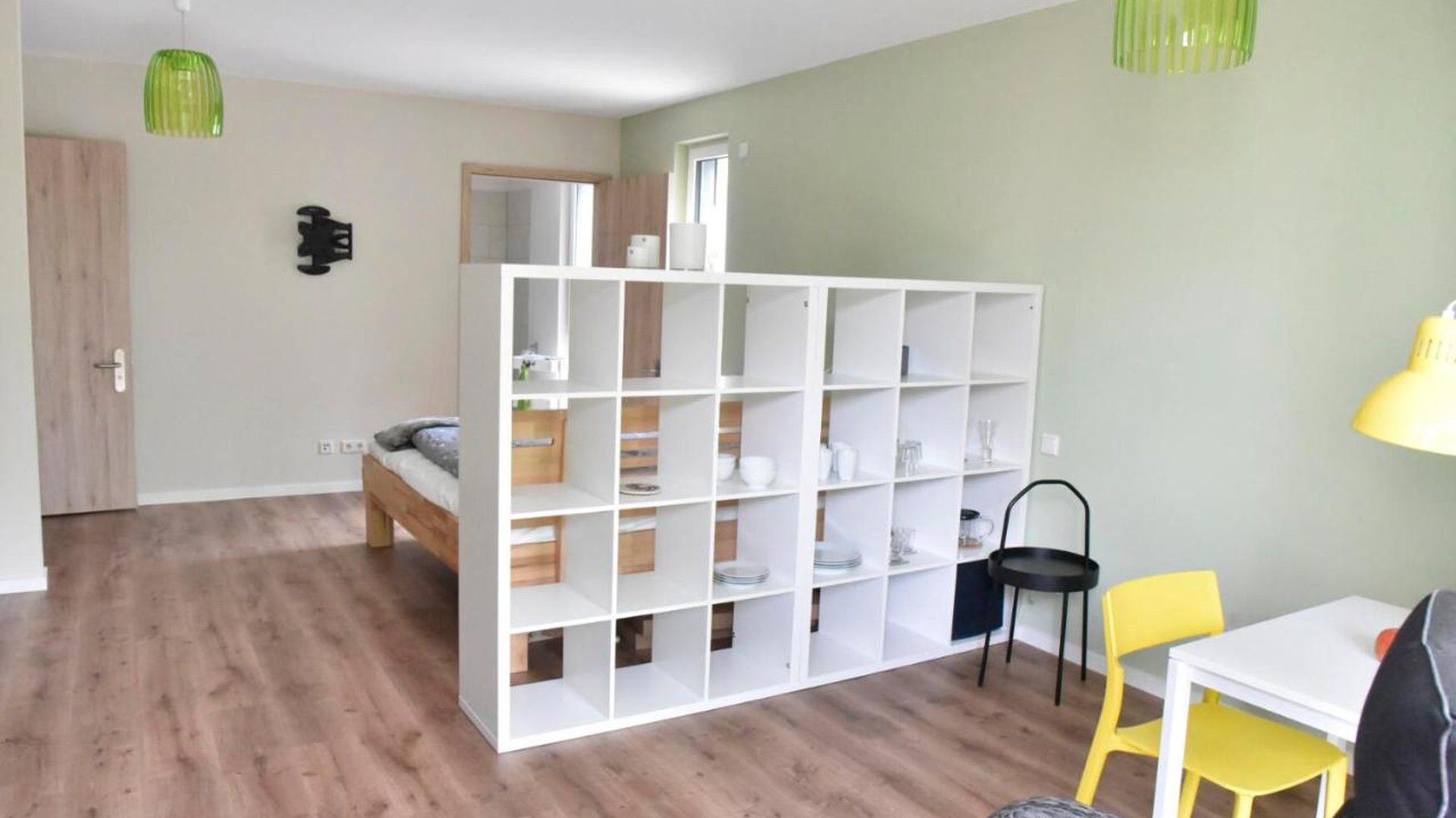 A room with a bed, a white shelving unit, a desk, and a chair.