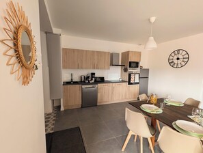 Eine moderne Küche mit Holzausbau, einem eingebauten Backofen und einer Essecke mit Tisch für zwei Personen.