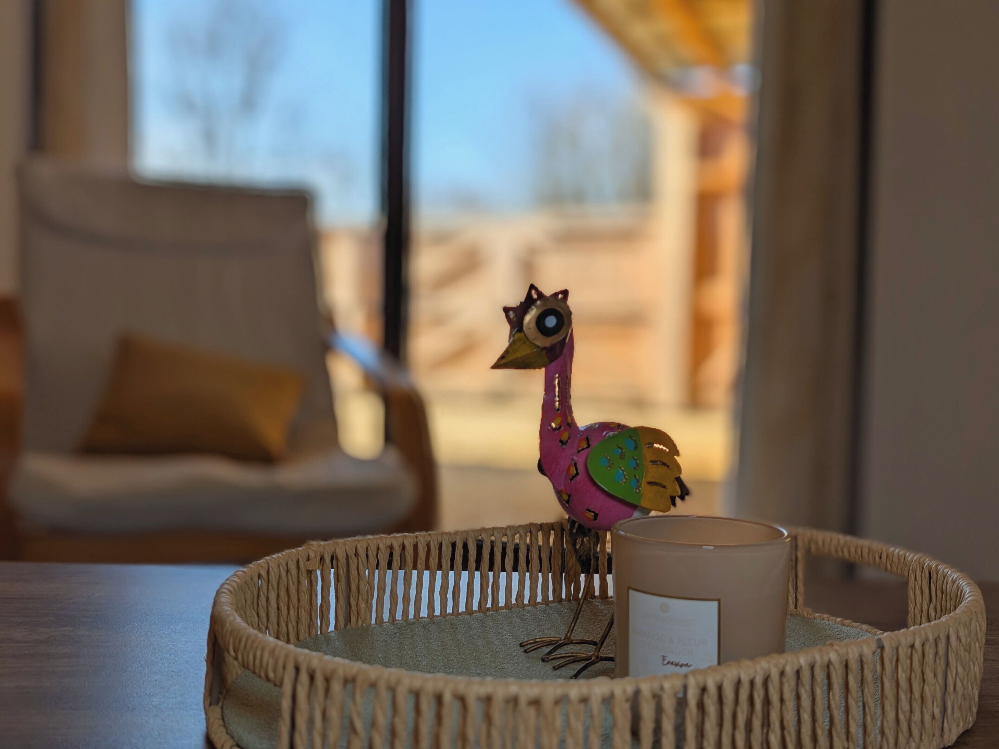 Ein Korbtablett mit einer dekorativen Vogelfigur und einer Kerze auf einem Tisch.