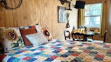 Um quarto com painéis de madeira, uma cama grande, um enfeite de bicicleta, uma mesa com cadeiras e uma janela.