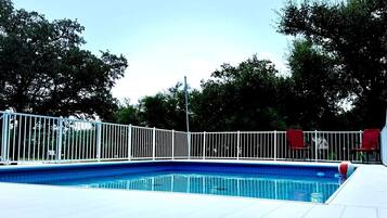 A swimming pool with a white fence, surrounded by trees.