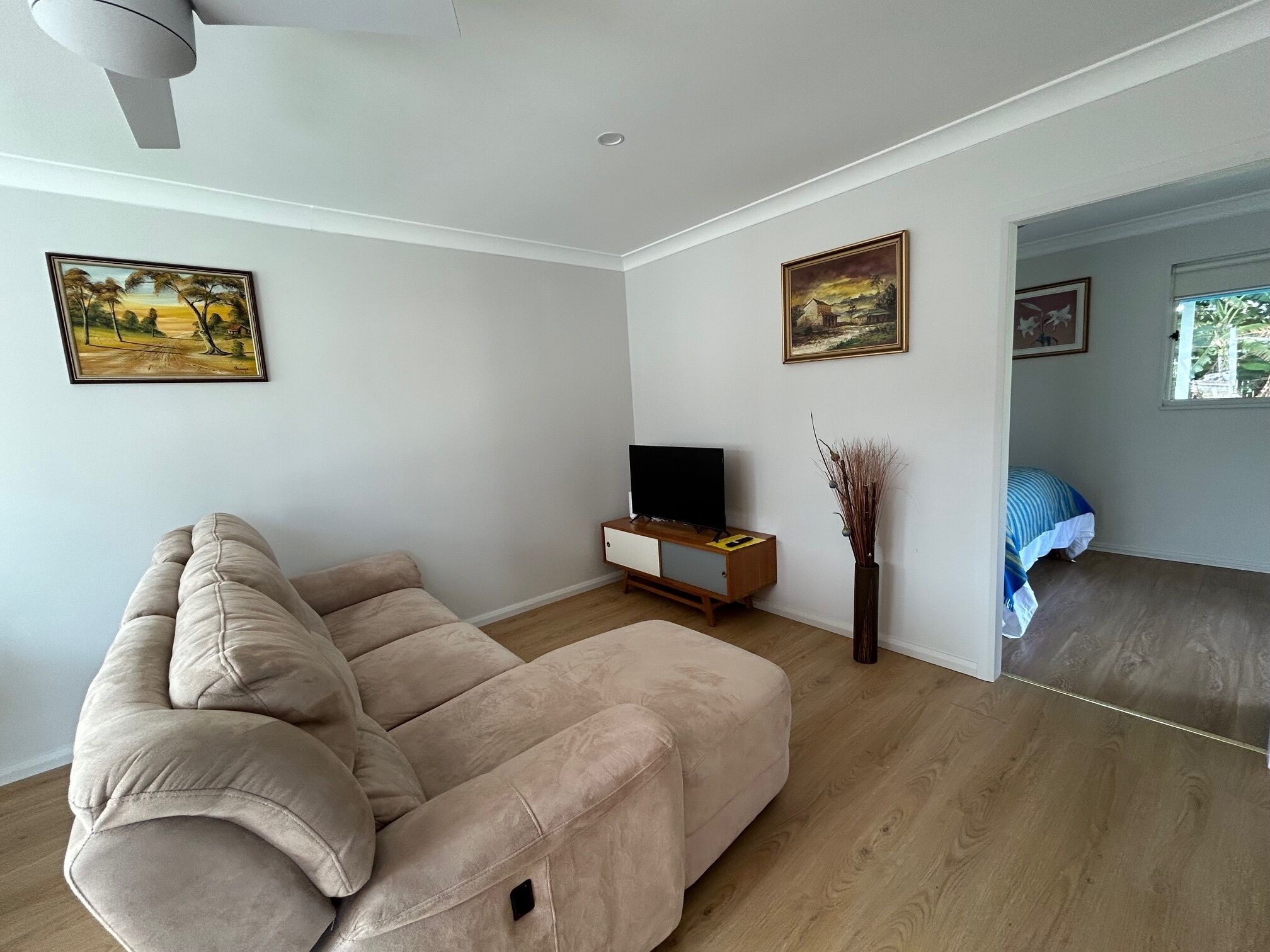 Un salon avec un canapé beige, un téléviseur pos é sur un meuble en bois et deux tableaux accrochés au mur.