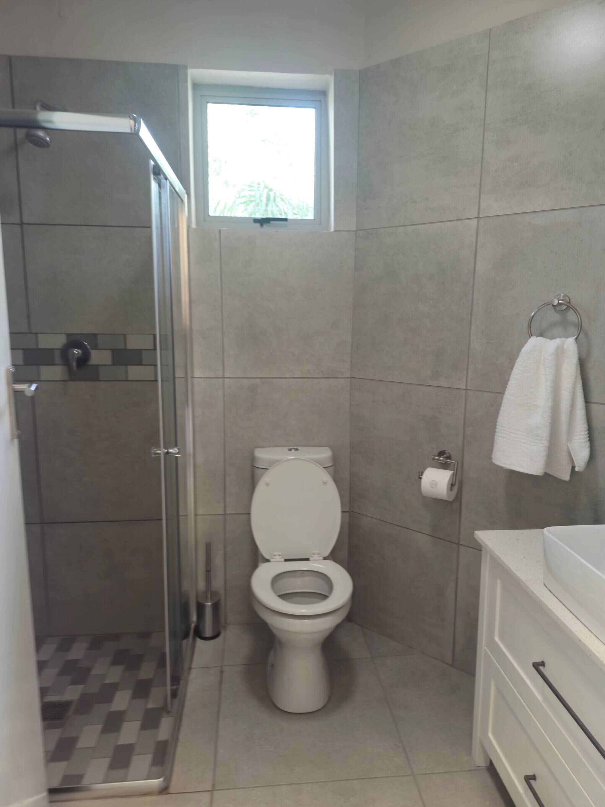 Ein Badezimmer mit Toilette, Dusche, Fenster und Waschbecken.