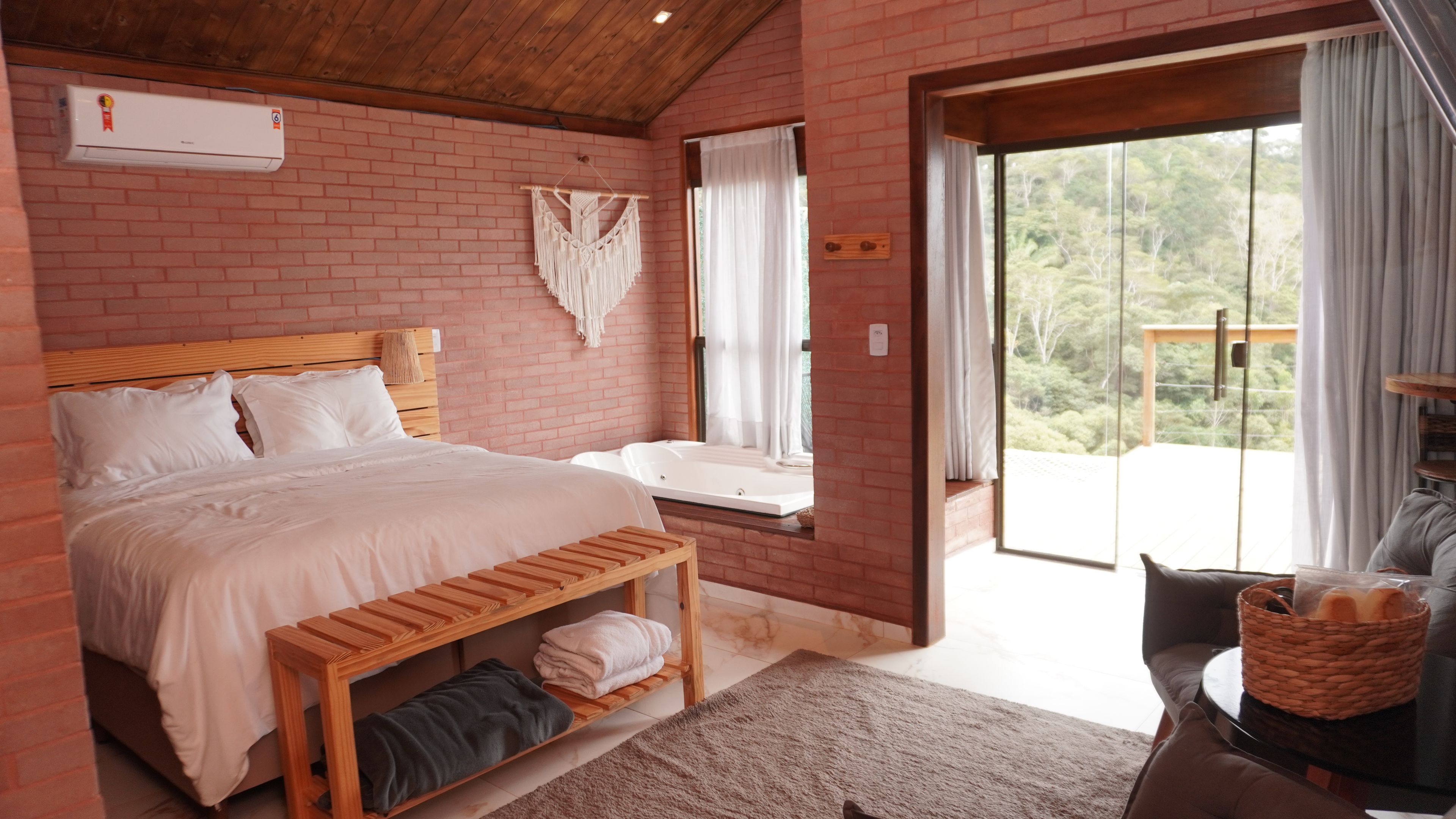 Un dormitorio con una cama de madera, un banco, una ventana con cortinas y vistas al exterior.
