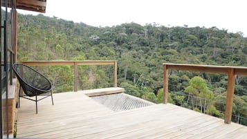 Um deck de madeira com uma cadeira e guarda-corpo, com vista para uma encosta arborizada.