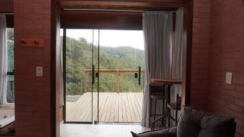 Una habitación con puerta corrediza de vidrio que da a una terraza de madera con vista a una colina boscosa.