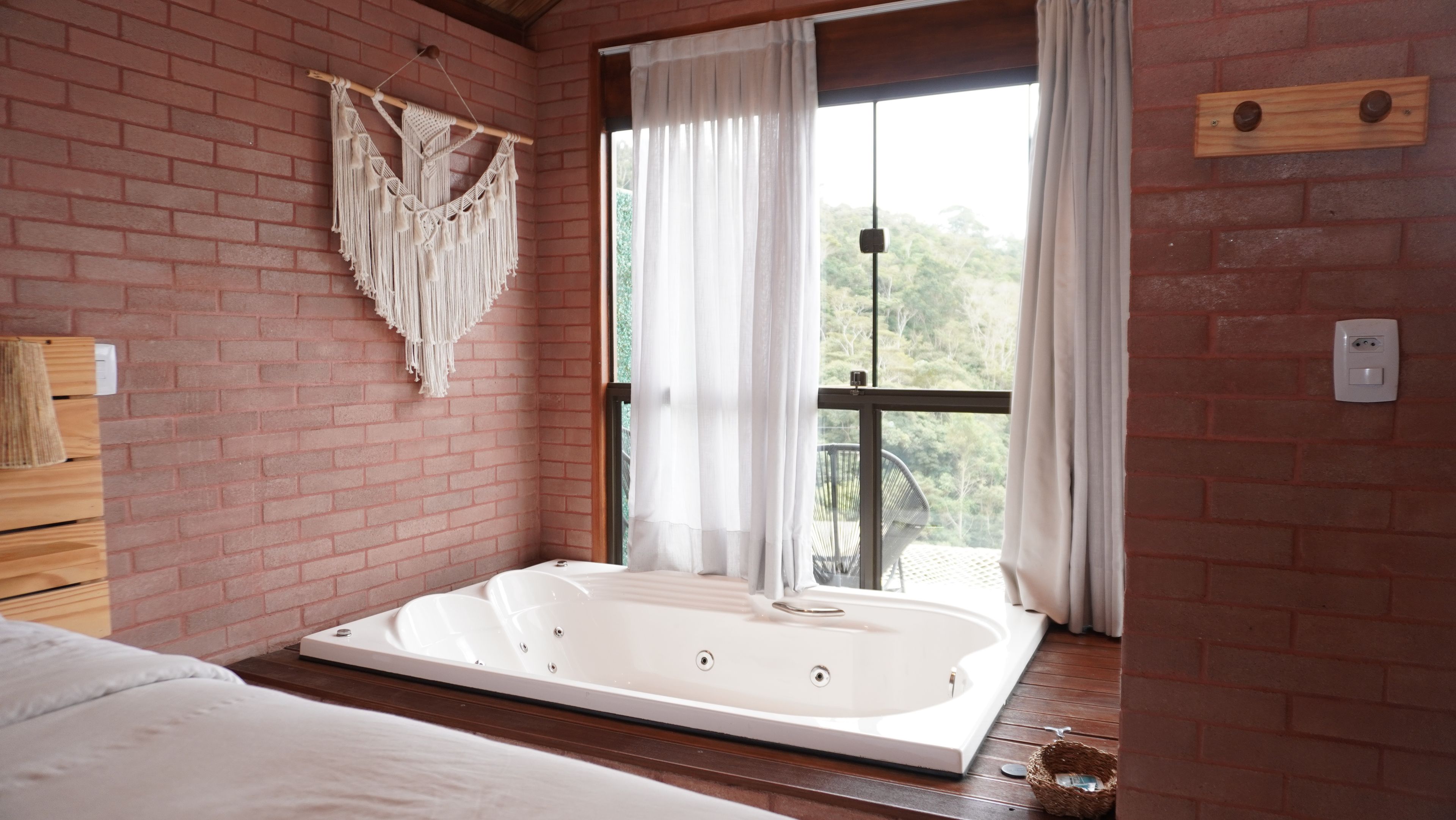 Une pièce dotée d’une grande baignoire, d’une décoration murale en macramé et offrant une vue à travers une porte-fenêtre coulissante.