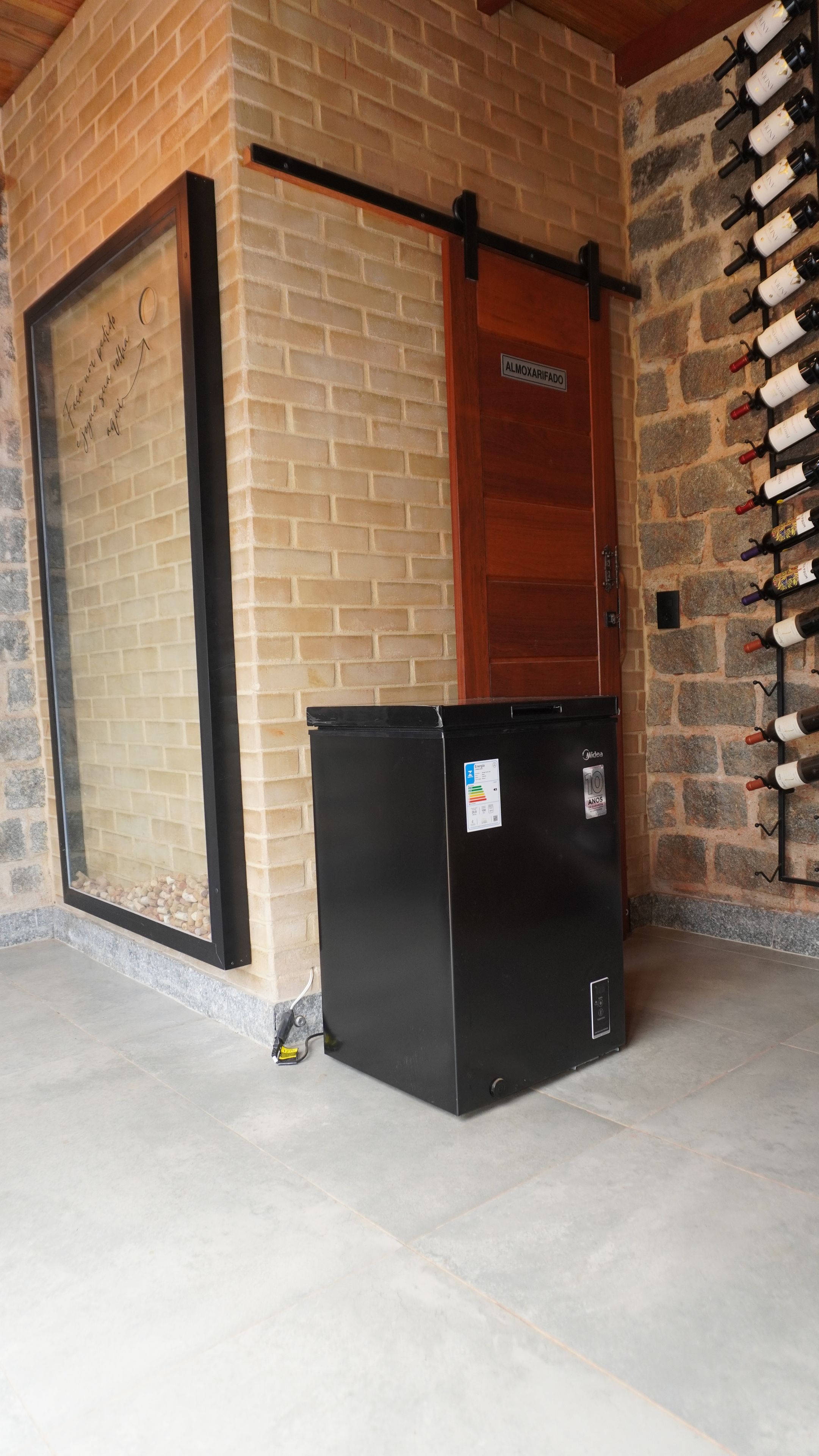 Una pared de ladrillo con una estantería para vinos y un refrigerador negro.
