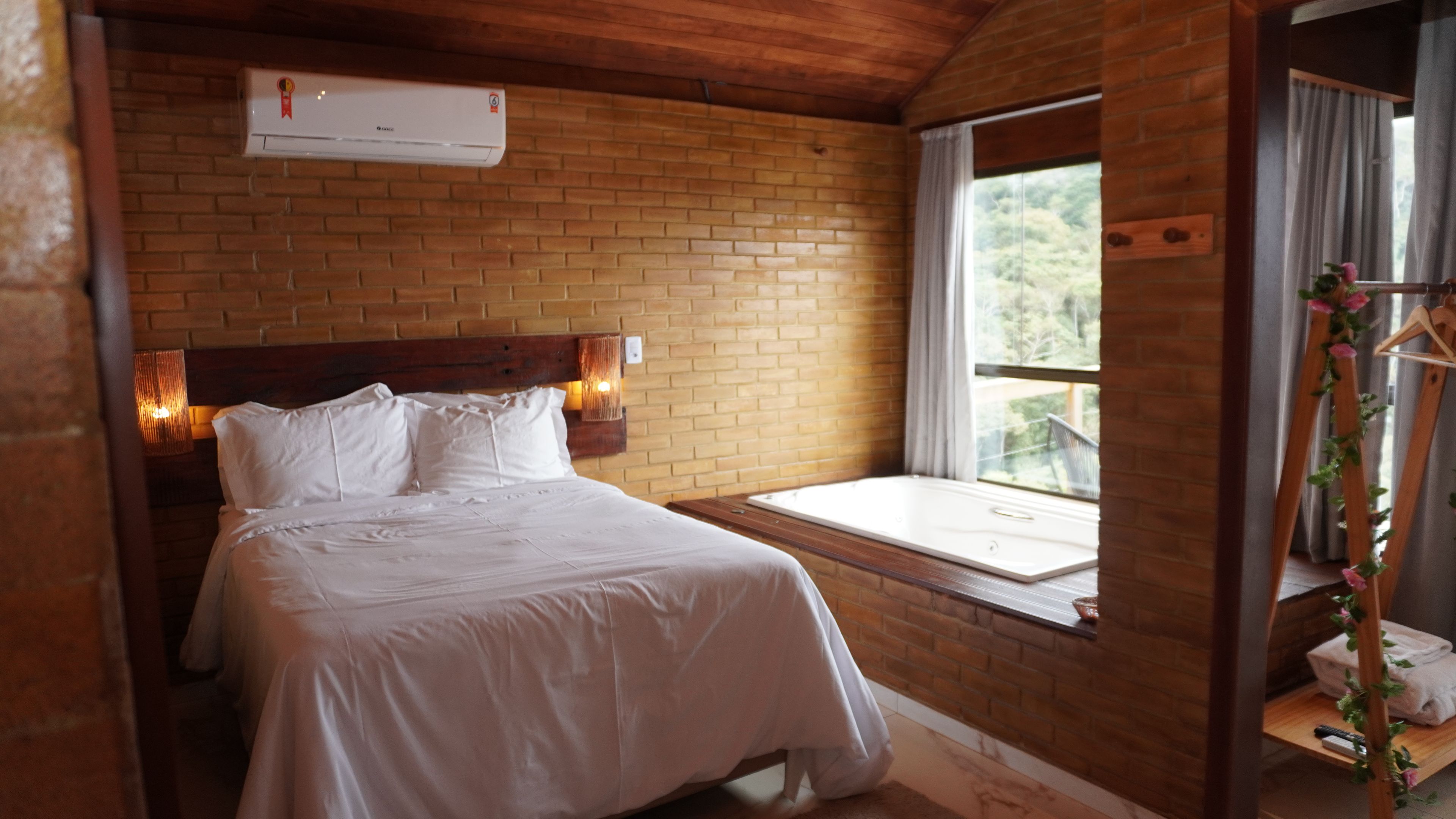 Un dormitorio con pared de ladrillo, cama con ropa blanca, ventana con vistas y cabecera de madera.