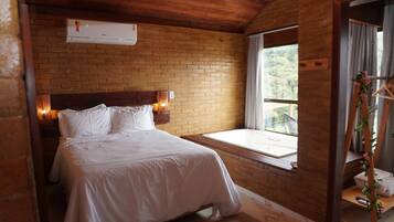 Un dormitorio con pared de ladrillo, cama con ropa blanca, ventana con vistas y cabecera de madera.