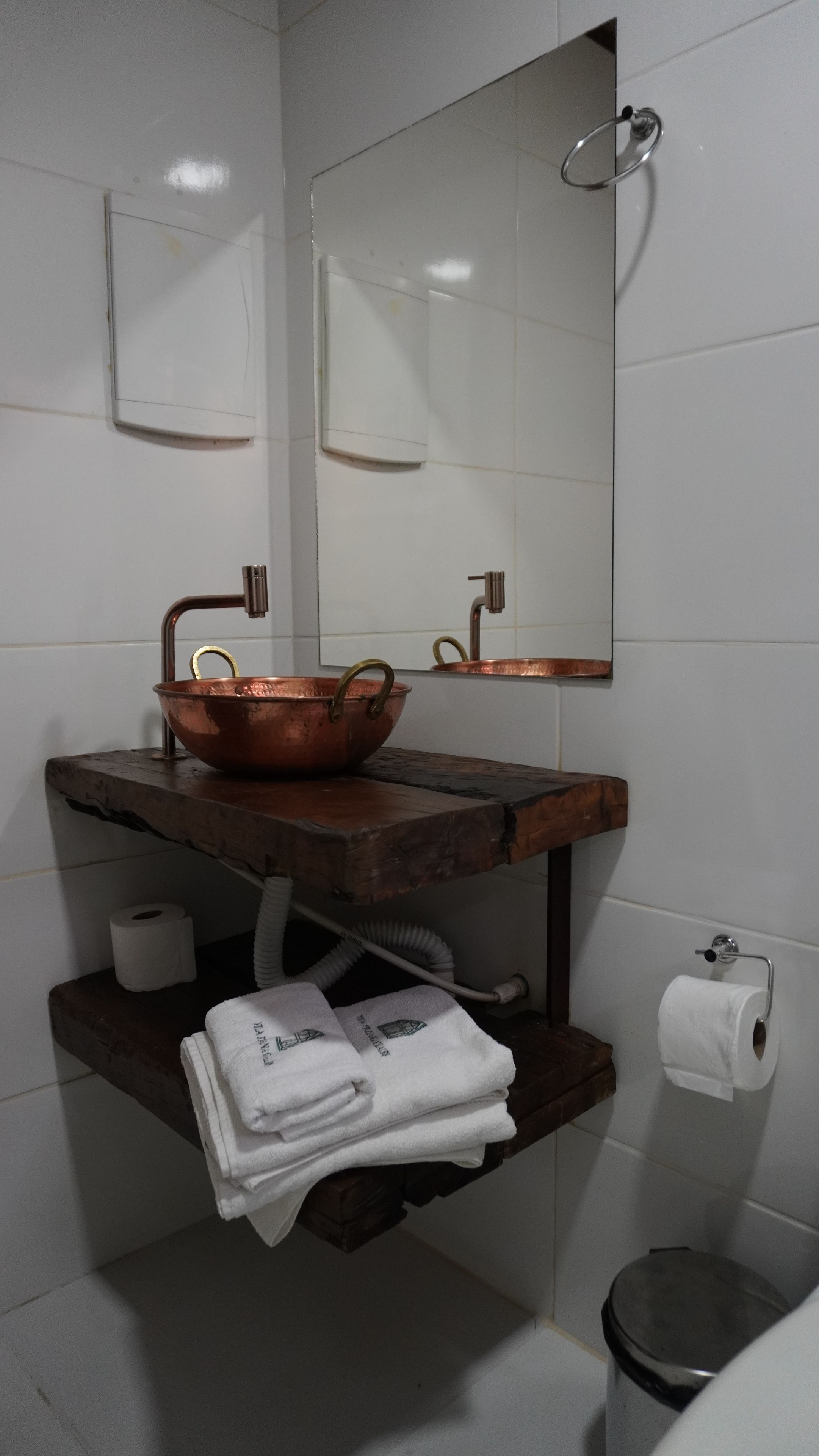 Une salle de bain avec un lavabo en cuivre, un miroir, un porte-serviettes et un support à papier toilette.