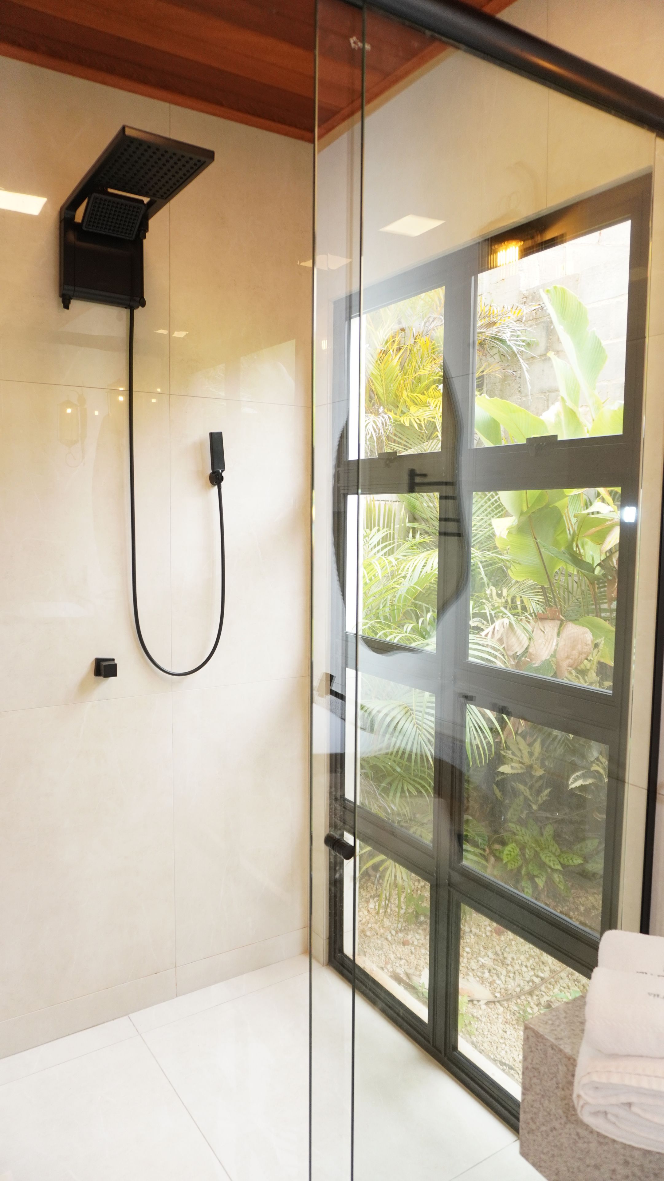 Un baño moderno con cabina de ducha de vidrio, ducha de mano y vistas al exterior.