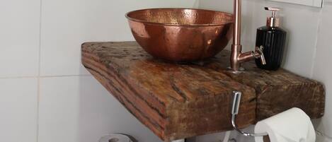 A bathroom with a copper basin, a faucet, a mirror, and a towel rack.