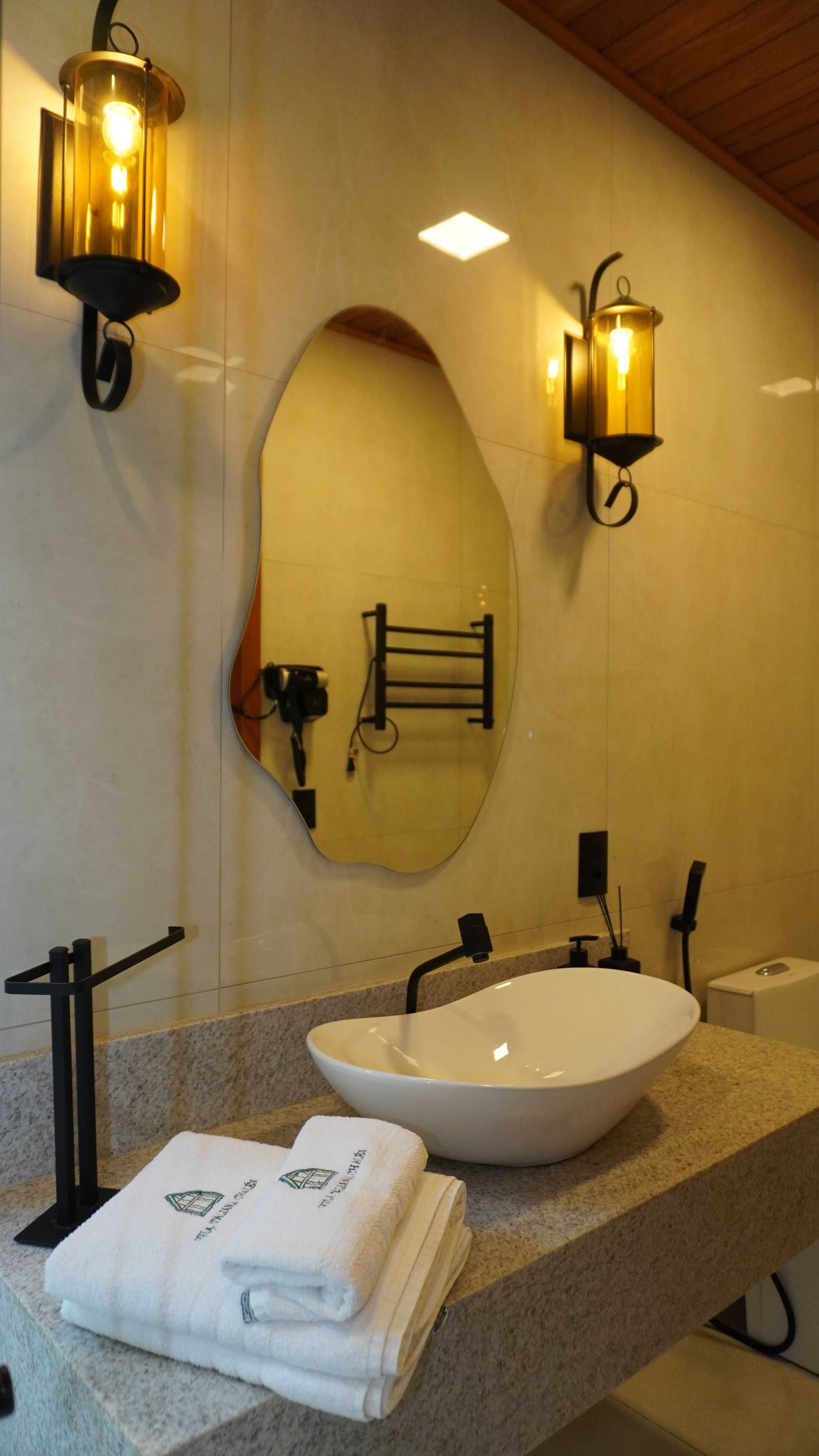 A bathroom with a large oval mirror, a white sink, and two wall-mounted lights.