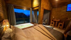 Una habitación con una cama grande, una ventana con cortinas, una mesita y un televisor en la pared.