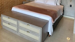 Un dormitorio con pared de ladrillo, techo de madera, cama con cabecera gris, lámparas de noche y un mueble de almacenamiento empotrado.