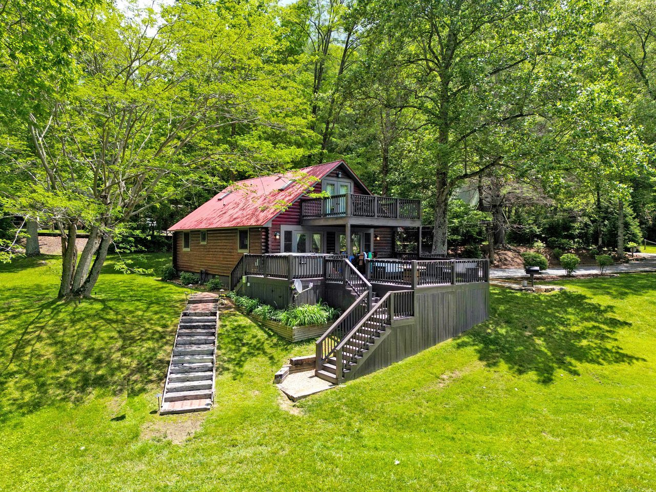 A cabin with a red roof, a deck, and a staircase leading to a porch.
