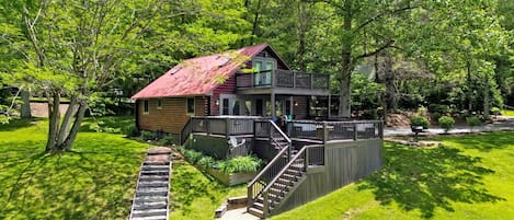 A cabin with a red roof, a deck, and a staircase leading to a porch.
