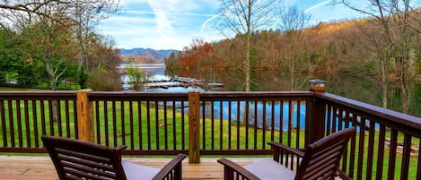 Une terrasse en bois avec deux chaises et une table, d’où l’on peut admirer un lac et des collines boisées.
